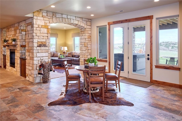 dining area with arched walkways, stone finish floors, baseboards, recessed lighting, and a stone fireplace
