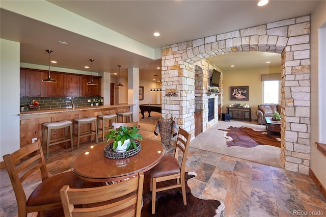 dining space featuring stone finish floors, a stone fireplace, recessed lighting, and arched walkways