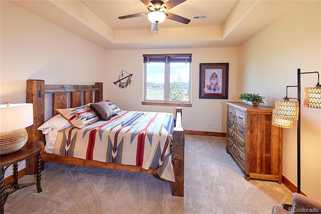 bedroom with light carpet, baseboards, a tray ceiling, and ceiling fan