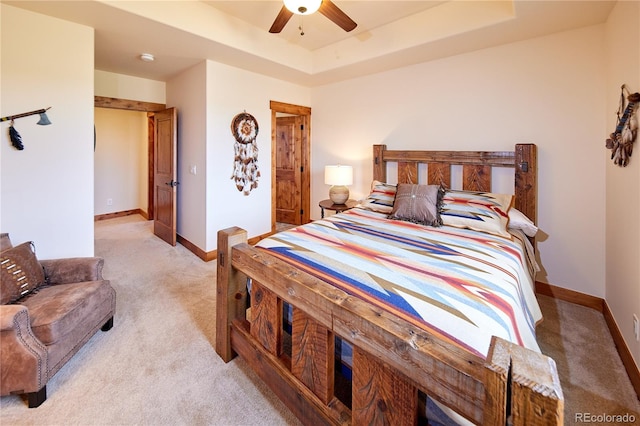 bedroom with light colored carpet, baseboards, a tray ceiling, and a ceiling fan