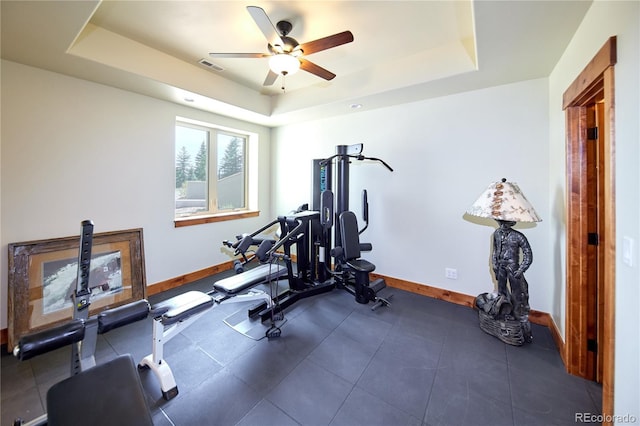 exercise area with baseboards, a tray ceiling, and ceiling fan
