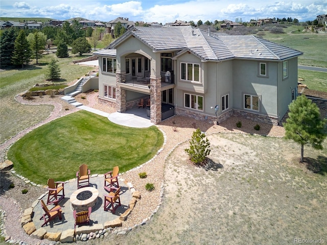 rear view of house featuring stone siding, stucco siding, a fire pit, and a patio