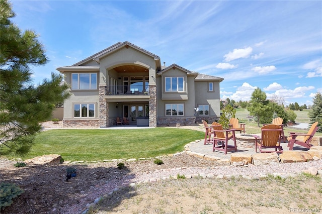 back of property with a balcony, stucco siding, an outdoor fire pit, a patio area, and stone siding
