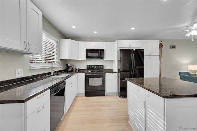 kitchen featuring sink, white cabinetry, light hardwood / wood-style flooring, dark stone counters, and black appliances