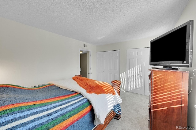 bedroom featuring light colored carpet, a textured ceiling, and two closets