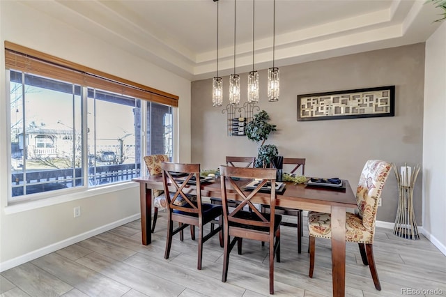 dining room featuring light hardwood / wood-style flooring, a raised ceiling, a chandelier, and a healthy amount of sunlight