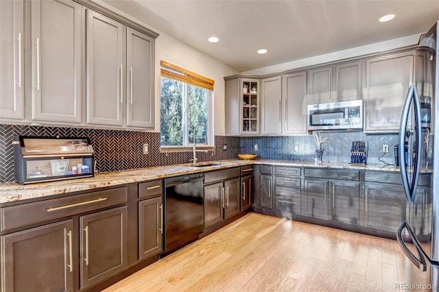 kitchen featuring appliances with stainless steel finishes, tasteful backsplash, light hardwood / wood-style floors, sink, and light stone counters