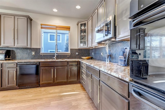 kitchen featuring backsplash, sink, black dishwasher, light hardwood / wood-style flooring, and light stone countertops