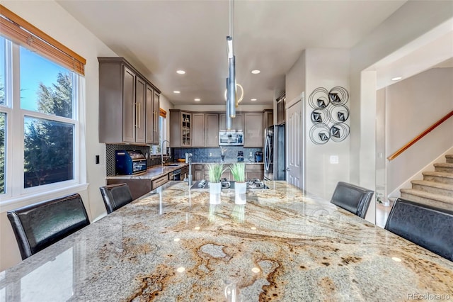 interior space with light stone countertops, appliances with stainless steel finishes, backsplash, hanging light fixtures, and a breakfast bar