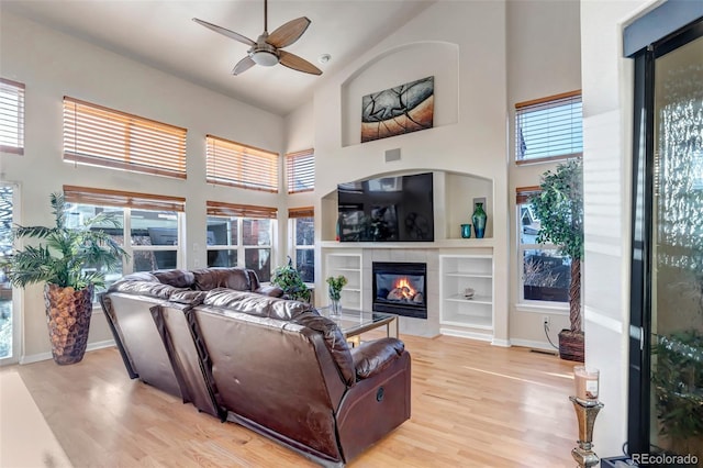 living room featuring ceiling fan, a fireplace, a towering ceiling, and light hardwood / wood-style floors