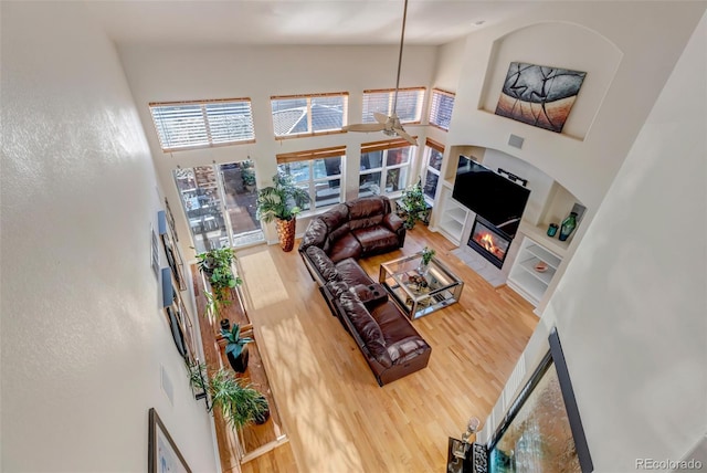 living room featuring ceiling fan, a fireplace, a high ceiling, and hardwood / wood-style flooring