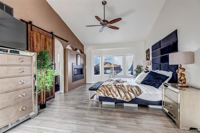 bedroom with ceiling fan, lofted ceiling, a barn door, and light hardwood / wood-style flooring