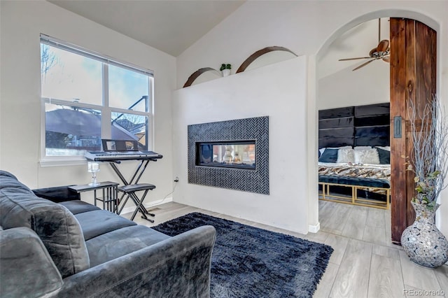 living room featuring light wood-type flooring, ceiling fan, lofted ceiling, and a tile fireplace