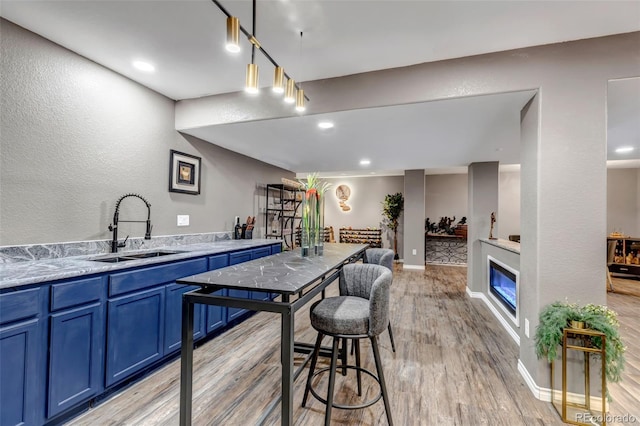 bar featuring light hardwood / wood-style floors, blue cabinetry, pendant lighting, light stone counters, and sink