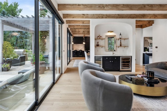 living room featuring beamed ceiling, light hardwood / wood-style floors, wet bar, and wine cooler