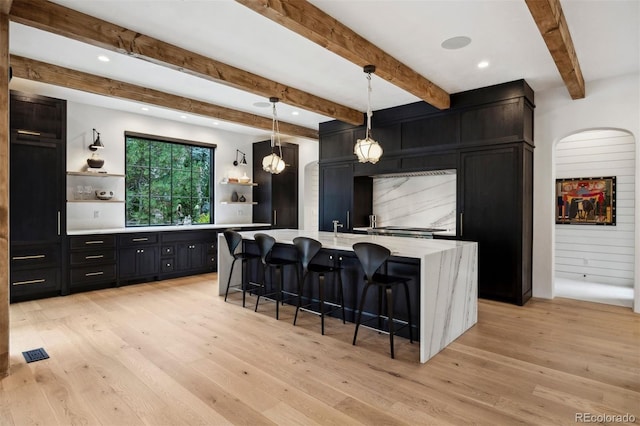 kitchen featuring a breakfast bar, an island with sink, hanging light fixtures, and light hardwood / wood-style flooring