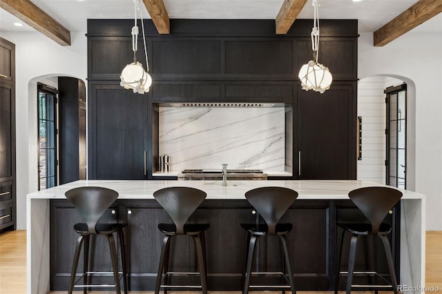 kitchen with light wood-type flooring, light stone counters, beamed ceiling, hanging light fixtures, and a breakfast bar area