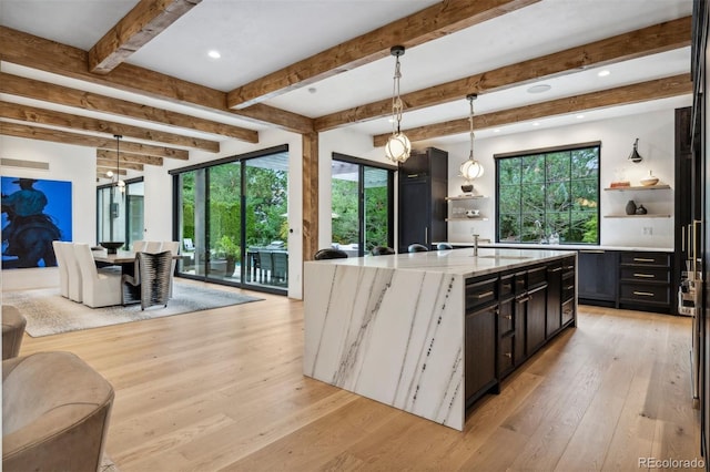 kitchen featuring sink, light stone counters, light hardwood / wood-style flooring, an island with sink, and decorative light fixtures