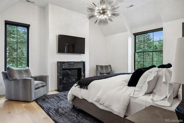 bedroom featuring vaulted ceiling, light hardwood / wood-style flooring, a high end fireplace, and a chandelier