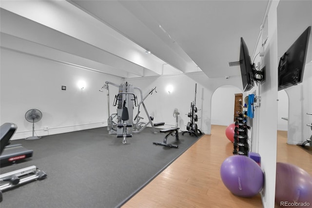 exercise room featuring arched walkways and wood finished floors