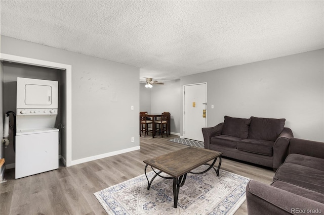 living room with stacked washer and dryer, a textured ceiling, ceiling fan, and light hardwood / wood-style flooring