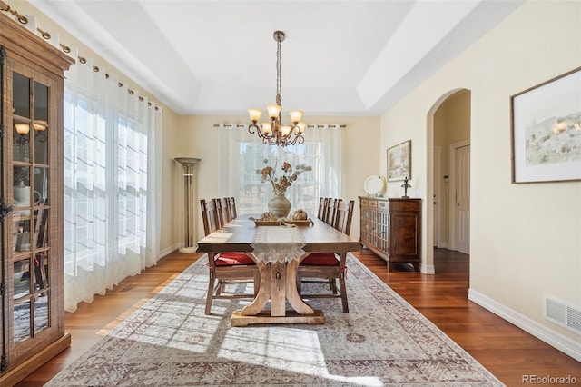 dining area with hardwood / wood-style flooring, a tray ceiling, and a notable chandelier