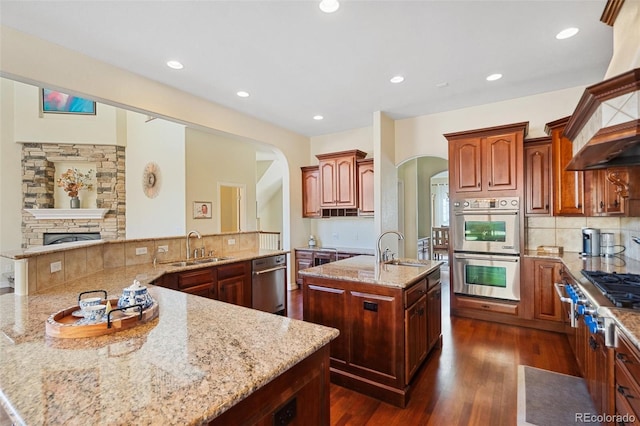 kitchen featuring light stone counters, appliances with stainless steel finishes, sink, and a center island with sink