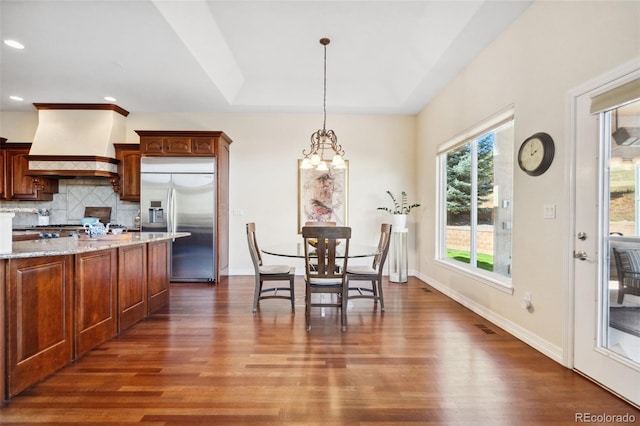 kitchen featuring premium range hood, tasteful backsplash, hanging light fixtures, dark hardwood / wood-style floors, and stainless steel built in fridge