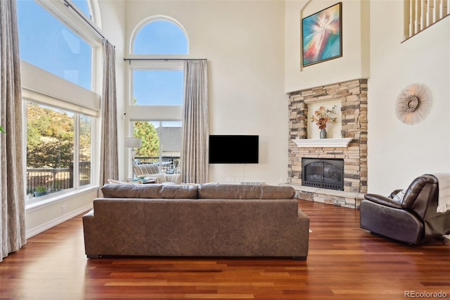 living room with hardwood / wood-style flooring, a stone fireplace, and a towering ceiling