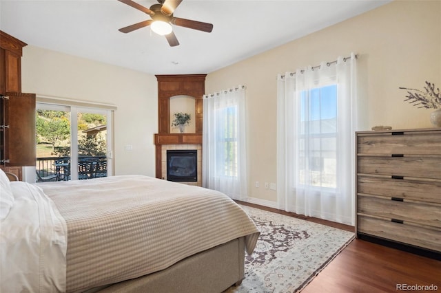 bedroom with a fireplace, dark wood-type flooring, access to outside, and ceiling fan