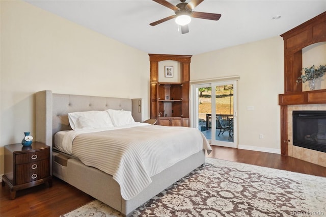 bedroom featuring dark hardwood / wood-style flooring, access to exterior, a tiled fireplace, and ceiling fan