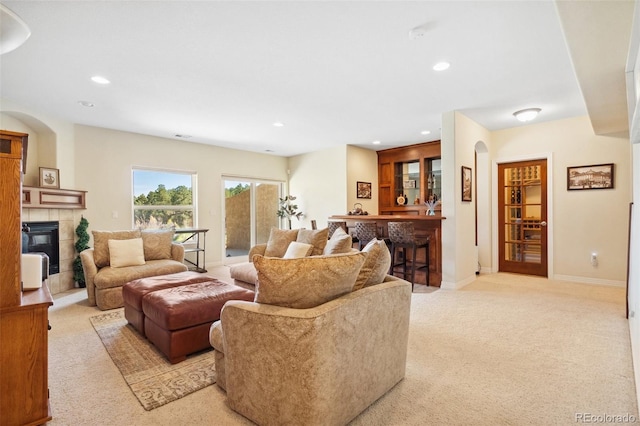 living room featuring a tiled fireplace, light carpet, and bar