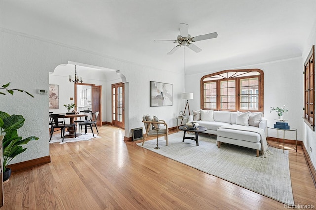 living room with arched walkways, light wood-type flooring, plenty of natural light, baseboards, and crown molding