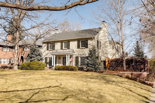 view of front of property featuring a front yard, a balcony, and a chimney