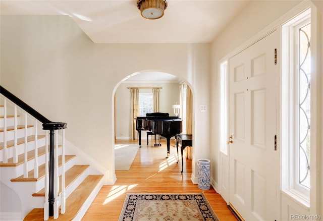 entryway with arched walkways, light wood-style flooring, stairs, and baseboards