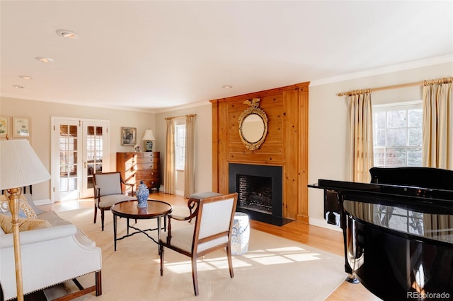 living room with french doors, a large fireplace, light wood-style floors, crown molding, and baseboards