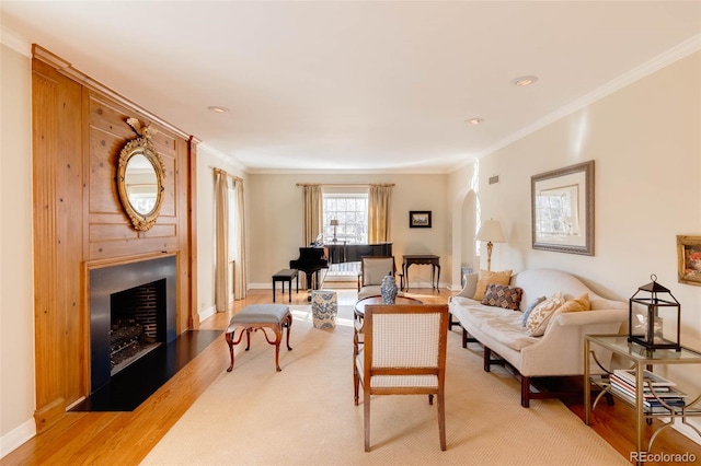 living area featuring crown molding, baseboards, light wood-type flooring, a fireplace, and arched walkways