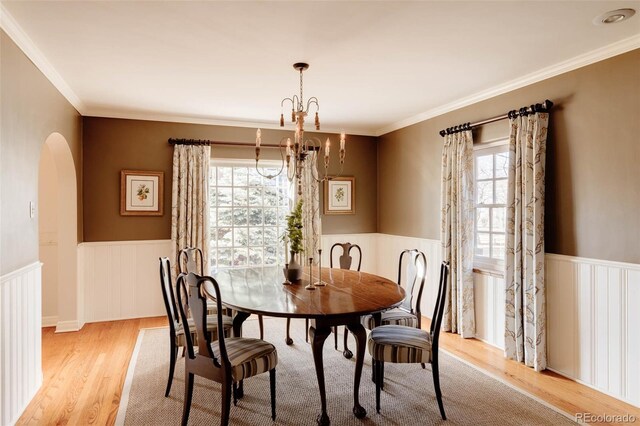 dining room with ornamental molding, arched walkways, wainscoting, light wood finished floors, and a chandelier