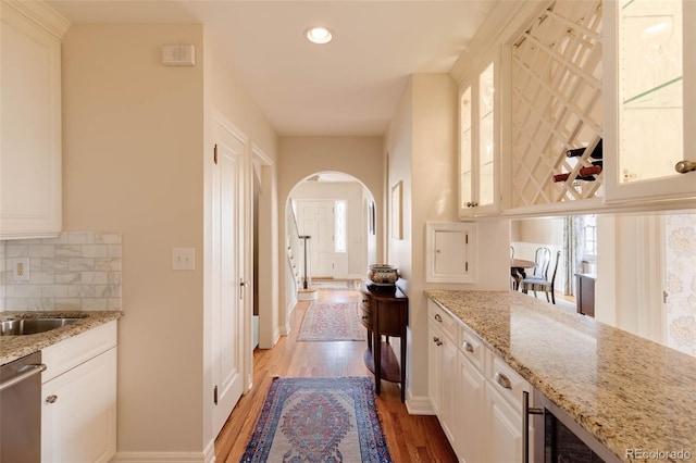 kitchen with tasteful backsplash, light wood-type flooring, arched walkways, white cabinets, and stainless steel dishwasher