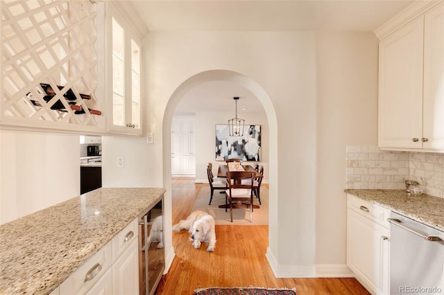 kitchen featuring light wood-type flooring, light stone counters, tasteful backsplash, arched walkways, and dishwasher