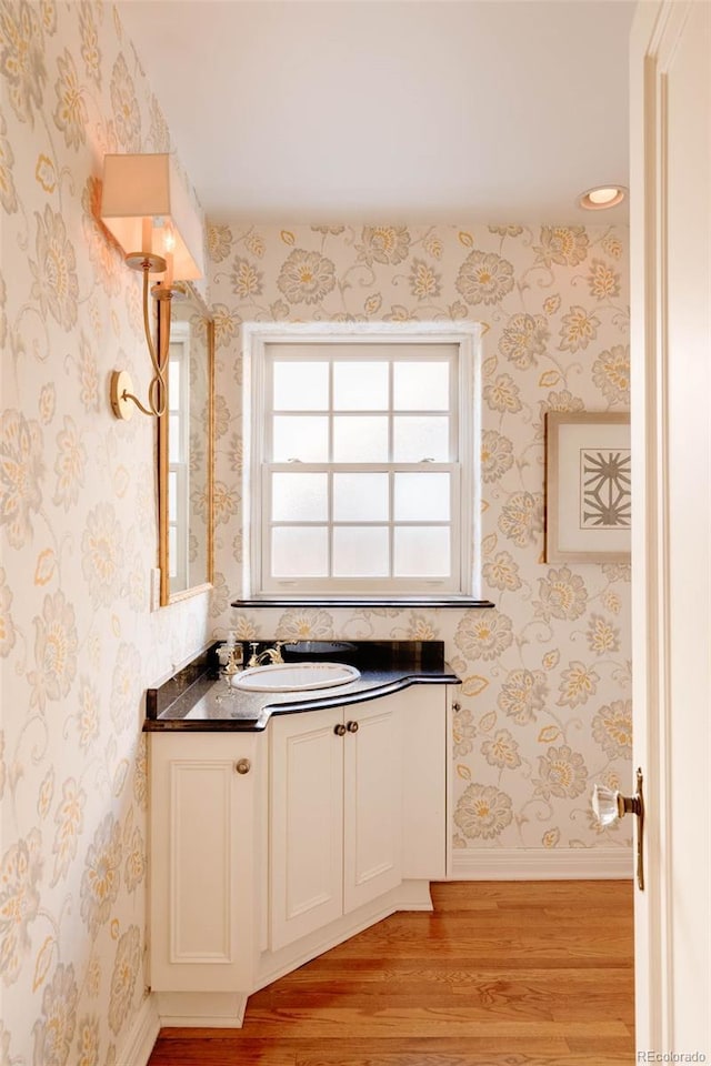 bathroom with wallpapered walls, vanity, baseboards, and wood finished floors