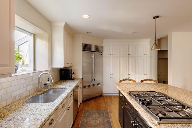 kitchen featuring light wood finished floors, decorative light fixtures, stainless steel appliances, white cabinetry, and a sink