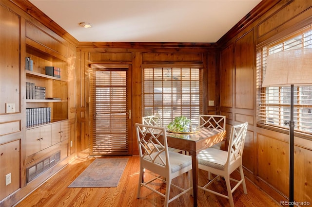 dining space featuring wooden walls, built in features, visible vents, and light wood-type flooring