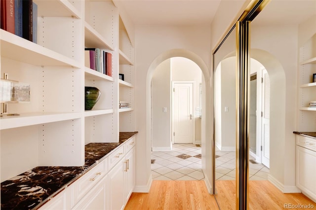 hallway featuring built in features, light wood-style floors, and arched walkways