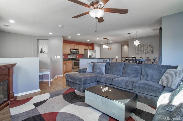 living room featuring light wood-style floors, recessed lighting, a fireplace with flush hearth, and ceiling fan with notable chandelier