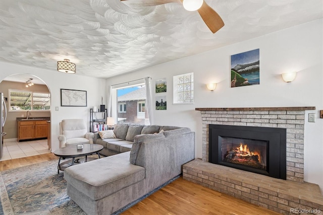 3154 N Columbine St, Denver, CO 80205 - living room with light wood-style flooring, ceiling fan, a brick fireplace, a textured ceiling, and arched walkways