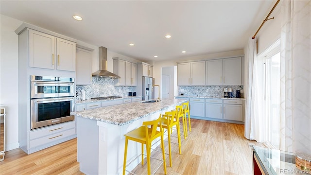 55 Morgan Cir, Erie, CO 80516 - kitchen with wall chimney range hood, appliances with stainless steel finishes, light wood-style flooring, decorative backsplash, and recessed lighting