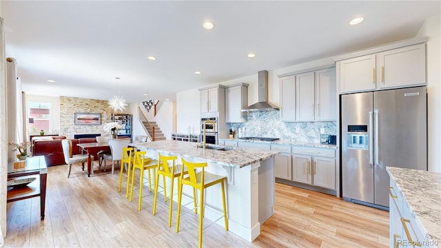 55 Morgan Cir, Erie, CO 80516 - kitchen featuring appliances with stainless steel finishes, wall chimney range hood, a fireplace, light wood-style floors, and recessed lighting