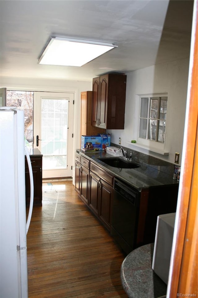 kitchen featuring dishwasher, dark countertops, dark wood-type flooring, freestanding refrigerator, and a sink