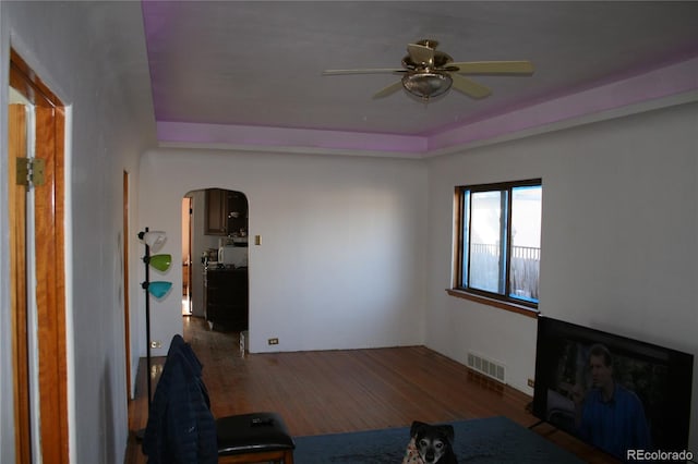 living room featuring a ceiling fan, arched walkways, visible vents, and wood finished floors